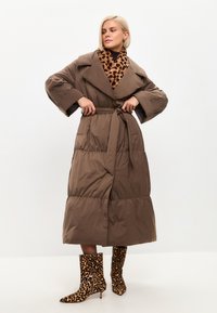 Piumino lungo marrone con ampio colletto e cintura, caratterizzato da dettagli in stampa leopardata. Il cappotto ha una texture trapuntata e due tasche laterali.