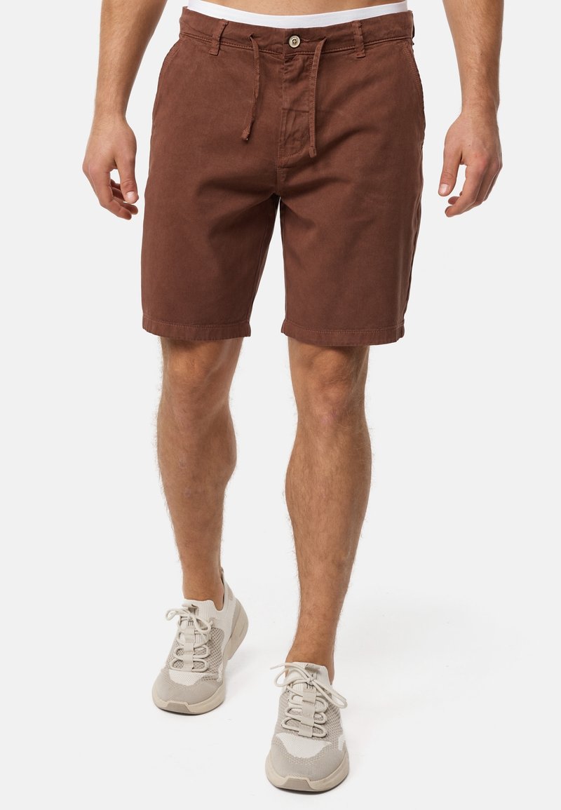 Shorts en coton marron avec cordon de serrage et fermeture par bouton, dotés de poches latérales et d'une coupe décontractée, assortis à des chaussures de sport gris clair.