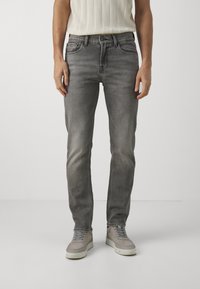 Jeans in denim grigio con un design aderente, cinque tasche e una leggera sfumatura. Abbinati a sneaker grigie chiare. La texture appare liscia con una brillantezza minima.