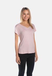 Bluzka z dekoltem w kształcie litery V i krótkim rękawem w miękkim różowym materiale, o luźnym kroju i subtelnej drapacji. Połączona z czarnymi dżinsami o dopasowanym kroju.