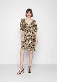 Vestido de estampado de leopardo em bege e preto; mangas curtas volumosas; decote em V profundo; até ao joelho; usado com saltos altos pretos com tiras. Textura suave.