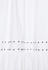 Tissu blanc avec couture froncée et deux rangées horizontales de petits clous argentés uniformément espacés au centre.