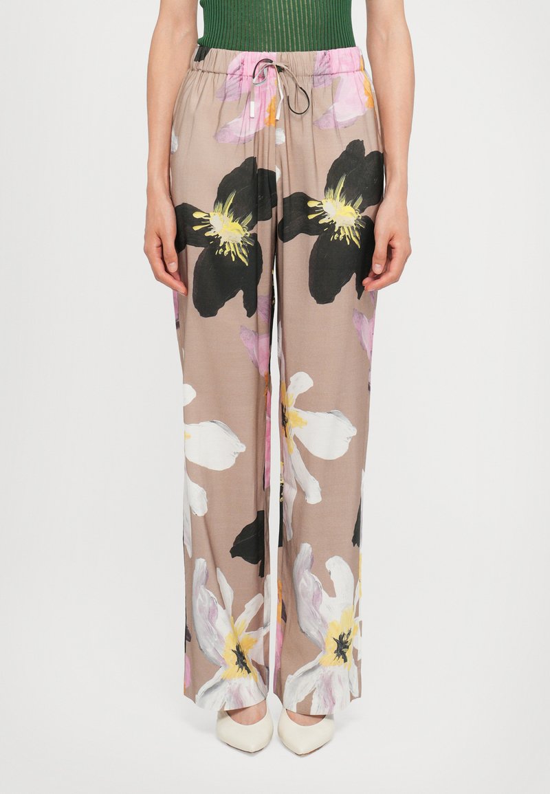 Pantaloni leggeri e fluidi in beige con grandi motivi floreali in nero, bianco e rosa; presentano una vita elasticizzata e un cordoncino.