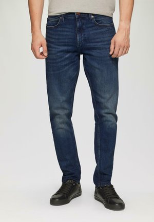 Dark blue denim jeans with a slim fit, featuring slight fading and a classic five-pocket design. Paired with black sneakers.