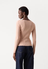 Top de manga larga de canalé en rosa claro, con un escote redondeado y un sutil detalle de costura en el hombro, combinado con pantalones de mezclilla oscuros.