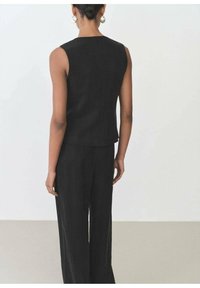 Černý bezramínkový top se střihováním rovného tvaru a strukturovaným materiálem. Zadní pohled ukazuje jemné detaily šití a čisté designové linie.