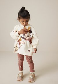 Kreemine dressipluus Minnie Mouse'i graafika ja sädelevate paeltega; kokku sobitatud roosa klõpsuvelgadega, millel on Minnie motiivid. Kanda jalatsitega.