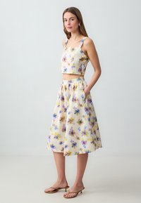 Zweiteiliges Outfit mit einem verkürzten Oberteil und einem langen Rock. Beide haben ein pastellfarbenes Blumenmuster auf einem hellen Hintergrund. Weicher Stoff.