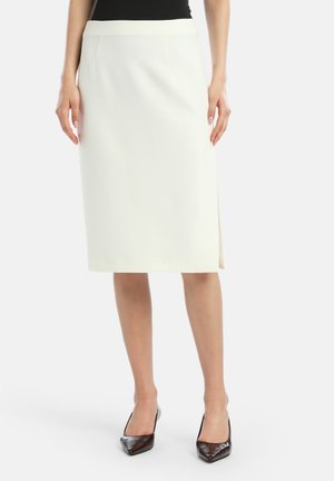 Weiße knielange Bleistifthose mit geradem Schnitt, ausgestattet mit einem seitlichen Schlitz und glatter Textur, kombiniert mit dunklen spitzen Absatzschuhen.