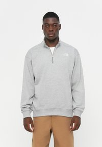 Pullover in felpa grigia con colletto a mezza zip, dotato di polsini e orlo a coste, e un piccolo logo bianco sul lato sinistro del petto.