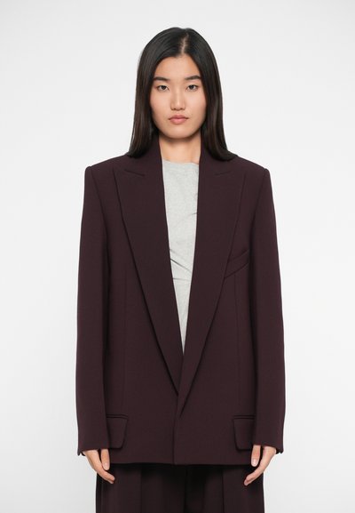 Burgundowy oversize blazer z wyraźnymi ramionami, klapami typu notch i dwiema przednimi kieszeniami, nałożony na szary top. Gładka faktura materiału.