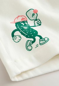 Cartone animato di un cetriolo con cappellino rosa e scarpe da ginnastica, che gioca a ping pong colpendo una pallina rosa con una racchetta su tessuto bianco.