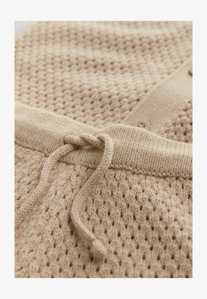 Veselă tricotată bej cu un model texturat, prezentând un șnur și detalii cu nasturi la guler. Material moale, țesut, cu o croială lejeră.