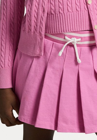 Rosa Kabelstrick-Cardigan kombiniert mit einem plissierten rosa Rock mit einem gestreiften Taillenbund und einem Kordelzug. Weicher Baumwollstoff.