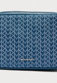 Μπλε υφασμάτινο πουγκί με γεωμετρικό μοτίβο από αλληλοσυνδεόμενα βέλη σε ανοιχτό μπλε. Ασημένια κείμενα γράφουν "MICHAEL KORS" στο κάτω μέρος.