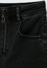 Svarta denimbyxor med dragkedjestängning och metalltriangel vid dragkedjan, framfickor och kontrasterande sömmar längs sömmarna.