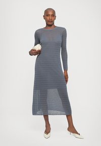 Rochie tricotată cu mânecă lungă, de culoare albastră deschisă, cu tiv în straturi și textură transparentă. Purtați cu o poșetă albă și pantofi cu vârful ascuțit.