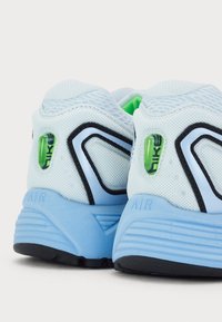 Chaussures de sport en mesh bleu et bleu clair avec des accents noirs, présentant un détail de logo vert et des semelles en caoutchouc texturées.