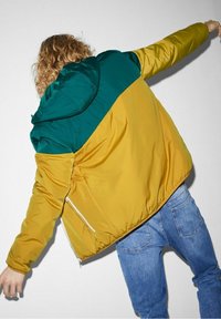 Colorblock-Steppjacke mit grünem Kapuzen und gelbem Körper, mit Reißverschluss und glatter, glänzender Stofftextur.