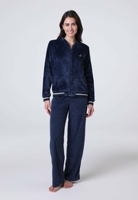 Tuta in velluto blu navy con giacca con zip, caratterizzata da un piccolo logo e bordi a costine a contrasto. Pantaloni larghi con gamba dritta.