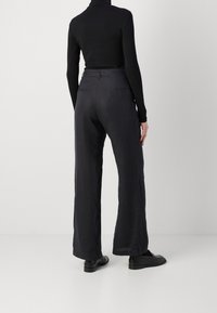 Svart polotröja i kombination med vida, mörkgrå byxor. Byxorna har en slät yta, rena linjer och diskreta fickor.