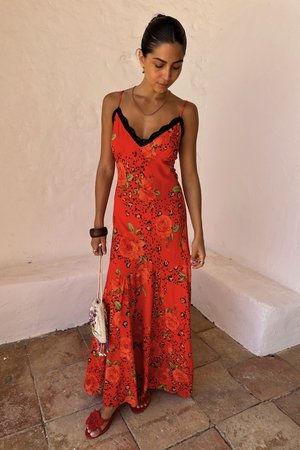 Rode bloemenmaxi-jurk met zwarte kanten halslijn, versierd met grote rozen en luipaardvlekken. Accessoires zijn een kleine tas en platte rode sandalen.