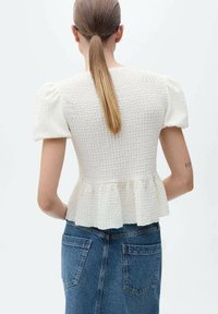 Top peplum bianco con effetto texturizzato, maniche a sbuffo e motivo intrecciato con orlo a balze. Abbinato a una gonna in denim a vita alta.