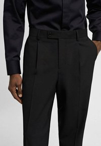 Czarne dopasowane spodnie wykonane z gładkiej tkaniny, z płaskim przodem, podwójnymi zakładkami i zapięciem na guzik w talii.