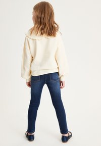 Felpa gialla chiaro con colletto a scallop, abbinata a jeans skinny blu scuro. Design semplice, texture morbida e senza motivi visibili.