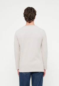 Φωτεινό μπεζ πουκάμισο με μακριά μανίκια, στρογγυλό ντεκολτέ και υφή υφάσματος, συνδυασμένο με τζιν παντελόνι. Ορατό στρίφωμα και χαλαρή εφαρμογή.