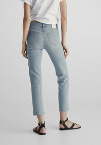 Light blue denim jeans with a straight cut, five pockets, and a stitched back yoke. Paired with black strappy sandals.