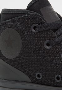 Černé plátěné sneakersy ve stylu high-top s texturovaným povrchem, kulatými tkaničkami a gumovou podrážkou. Obsahují kulatou nášivku s logem a kovové očka.