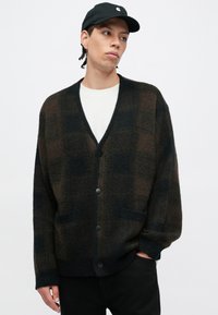 Tmavohnedý a čierno-károvaný sveter na zapínanie s véčkovým výstrihom, prednými vreckami a zapínaním na gombíky, vyrobený z mäkkého textúrovaného materiálu.