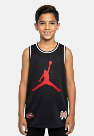 Ragazzo sorridente, che indossa una canotta da basket nera senza maniche con un grande logo rosso Jumpman e la scritta "Jordan" sul davanti.