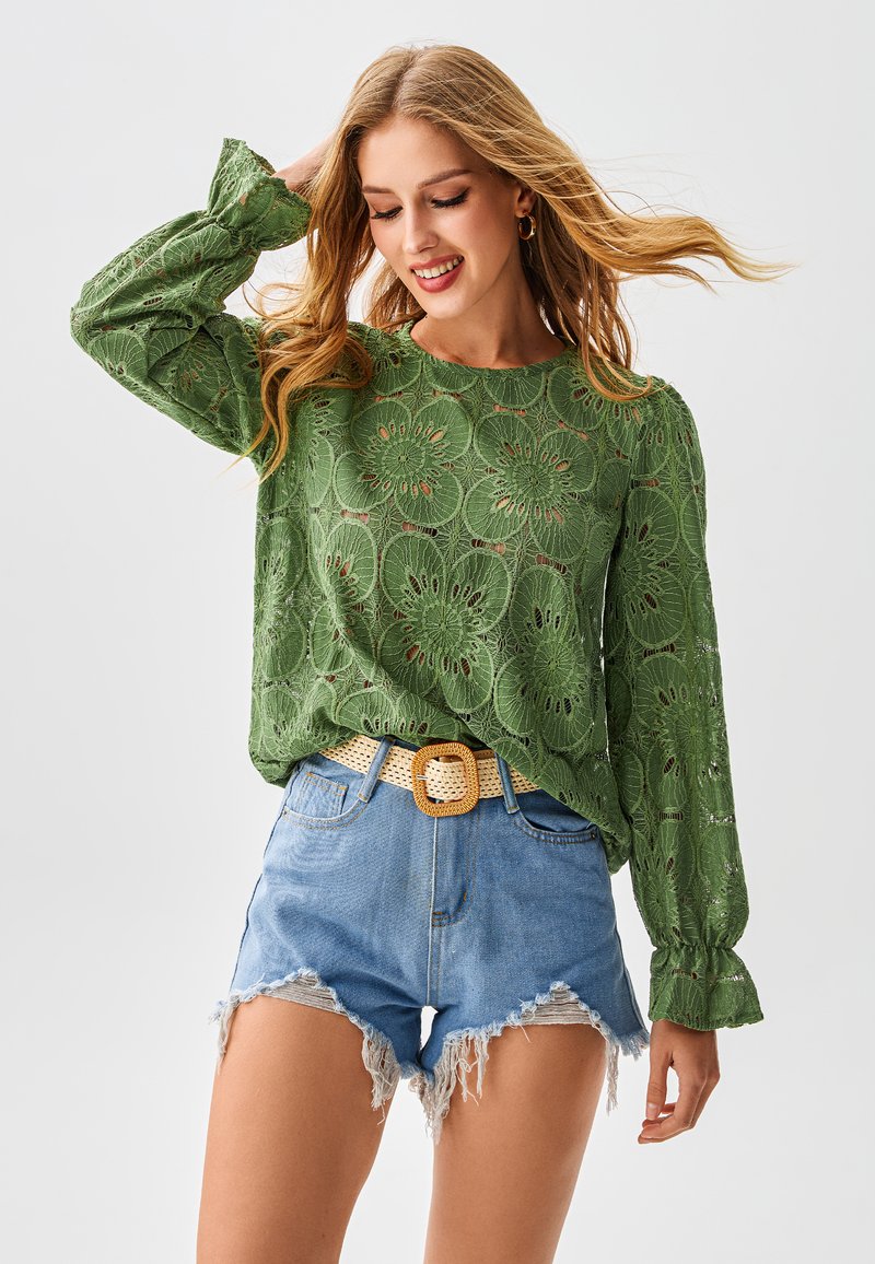 Groen kanten top met bloemenpatronen, lange mouwen en een ronde halslijn, gecombineerd met lichtblauwe gescheurde denim shorts en een geweven beige riem.