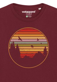 T-shirt bordeaux avec un motif circulaire de montagnes et d'arbres stylisés sur des rayures horizontales dans des dégradés de nuances d'orange, de rouge et de vert.