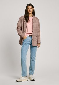 Blazer de cuadros marrón sobre un suéter rosa, combinado con jeans de un azul claro y zapatillas beige, con botones redondos y un corte relajado.
