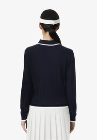 Pull en jersey marine avec des accents de col blanc, manches longues et une coupe ajustée, associé à une jupe plissée blanche.