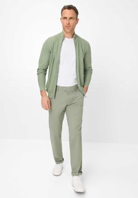 Light green zip-up cardigan over a white t-shirt, paired with light green trousers and white sneakers. Soft texture and slim fit.