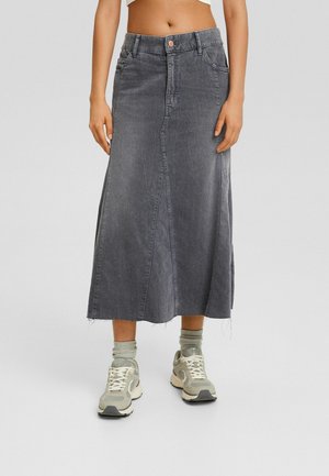 Woman wearing a faded gray midi denim skirt paired with light gray socks and white-gray sneakers, standing on a plain background.