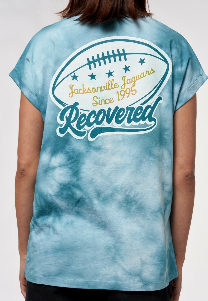 Ljusblått tie-dye t-shirt med en fotbollsillustration och texten "Jacksonville Jaguars Sedan 1995" samt ordet "Recovered" i fet stil.