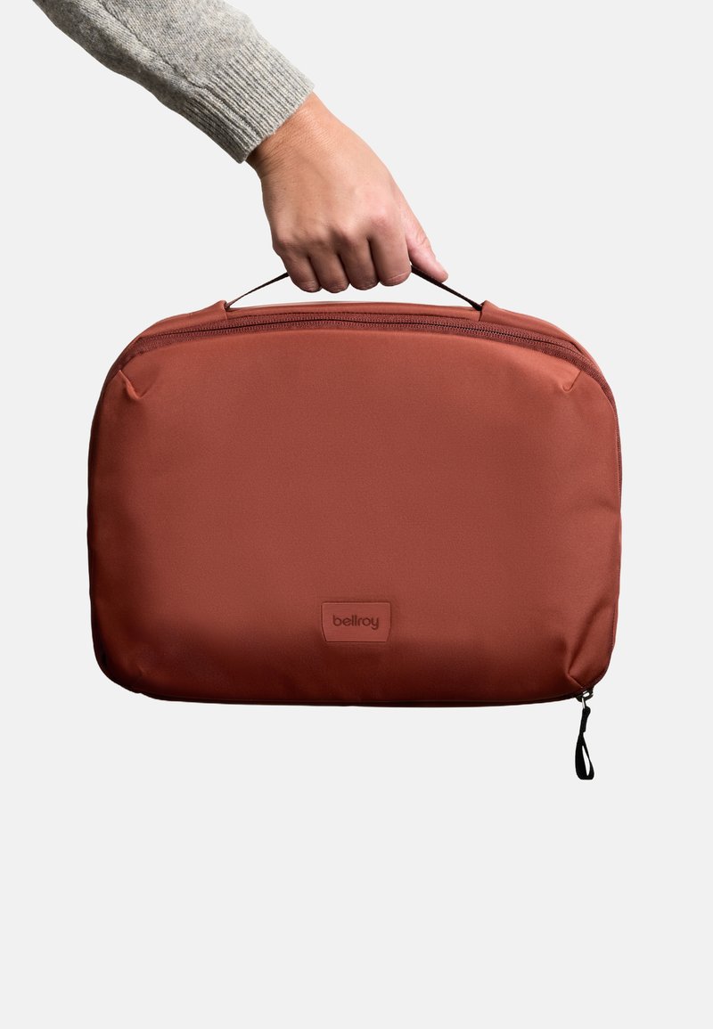 Custodia per laptop Bellroy in tessuto marrone rossiccio, chiusura con zip, manico superiore, texture liscia, logo sulla parte anteriore, design minimalista.