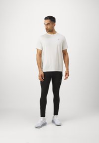 Jasnoszara koszulka sportowa, czarne legginsy i białe buty do biegania. Koszulka ma subtelne logo na piersi; legginsy dobrze przylegają.
