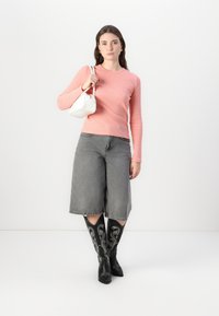 Top rosa a maniche lunghe e costine abbinato a culotte in denim grigio e stivali neri al ginocchio con ricami floreali bianchi. Borsa bianca in mano.