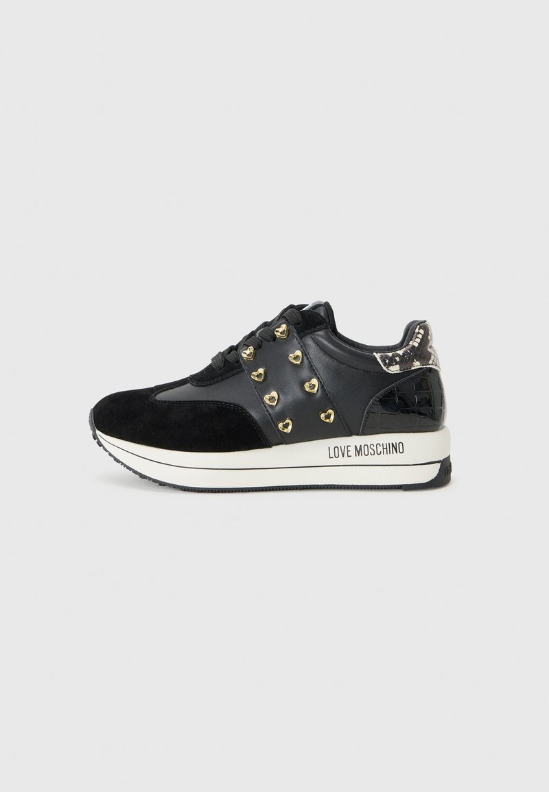 Zwarte suède en lederen sneaker met gouden hartstuds, gestructureerde hak en een witte tussenzool met "LOVE MOSCHINO" gedrukt.