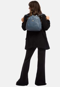 Blauwe leren rugzak met een gestructureerde afwerking, twee verstelbare schouderbanden, gouden hardware-accenten en een compacte, ronde vorm.