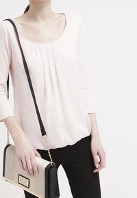 Helles rosa Blusenshirt mit einem Rundhalsausschnitt und dreiviertellangen Ärmeln, kombiniert mit einer strukturierten Clutch in Beige und Schwarz.