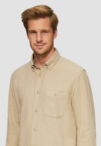 Beige Hemd mit Knöpfen aus einem strukturierten Stoff, ausgestattet mit einer Brusttasche, einem Kragen und dezenten Nähdetails. Lässig geschnittenes Design.