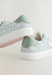 Glitzernde silberne Sneakers mit grünen Wildlederakzenten und weißen Gummisohlen; verfügen über eine strukturierte Oberfläche und ein Sternmotiv an der Seite.