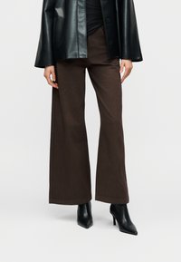 Καφέ φαρδιά παντελόνια από βαμβακερό μείγμα ύφασμα, με λεία υφή και καθαρό τελείωμα. Συνδυασμένα με μαύρα ψηλοτάκουνα παπούτσια με μυτερή μύτη.